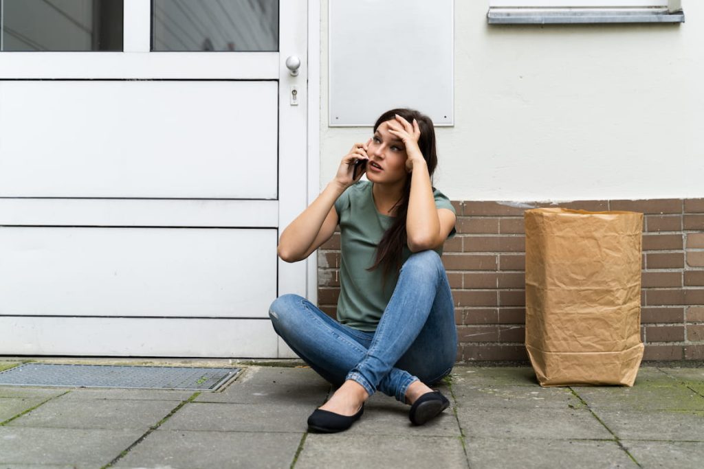 An Afraid Young Woman Sitting Outside The Door Talking On Mobilephone